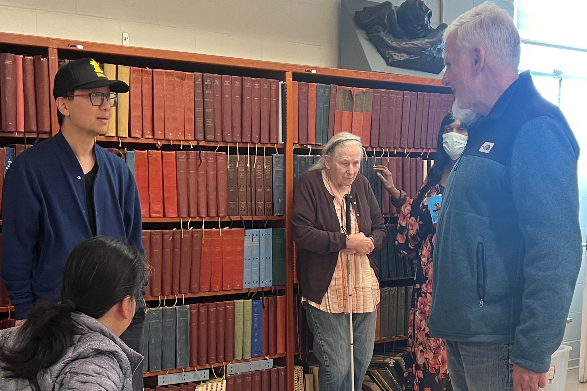 Group of people, some with white canes, in a library setting with bookshelves in the background