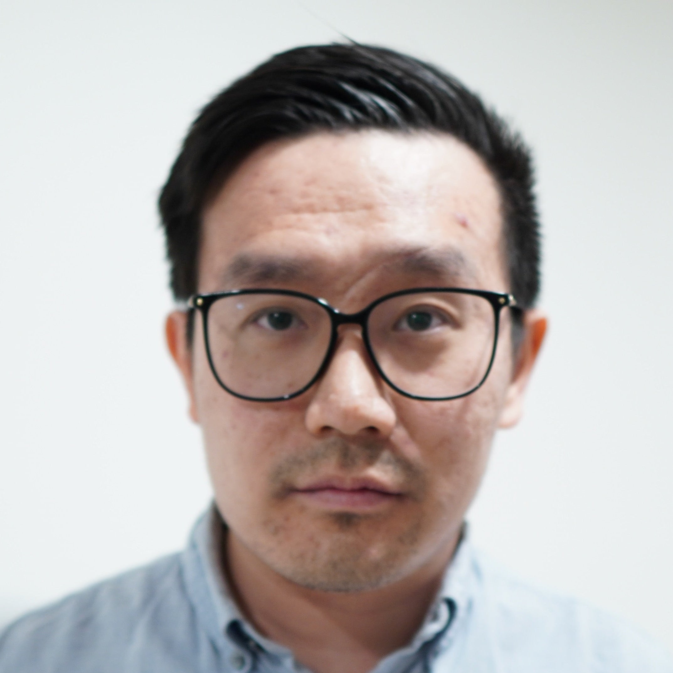 Man wearing glasses and a light blue shirt against a plain background