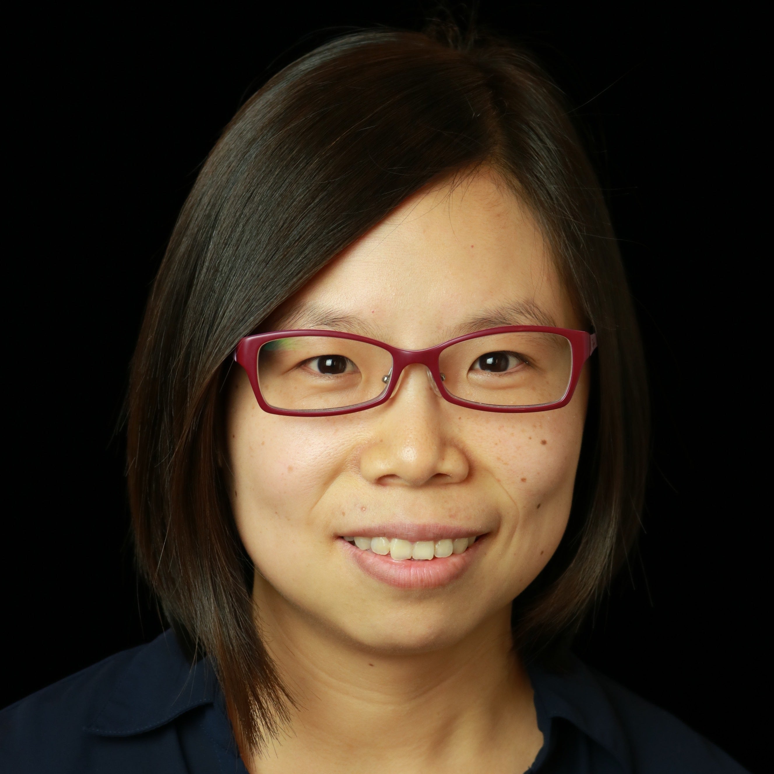 Woman wearing red glasses and a dark blue shirt against a black background